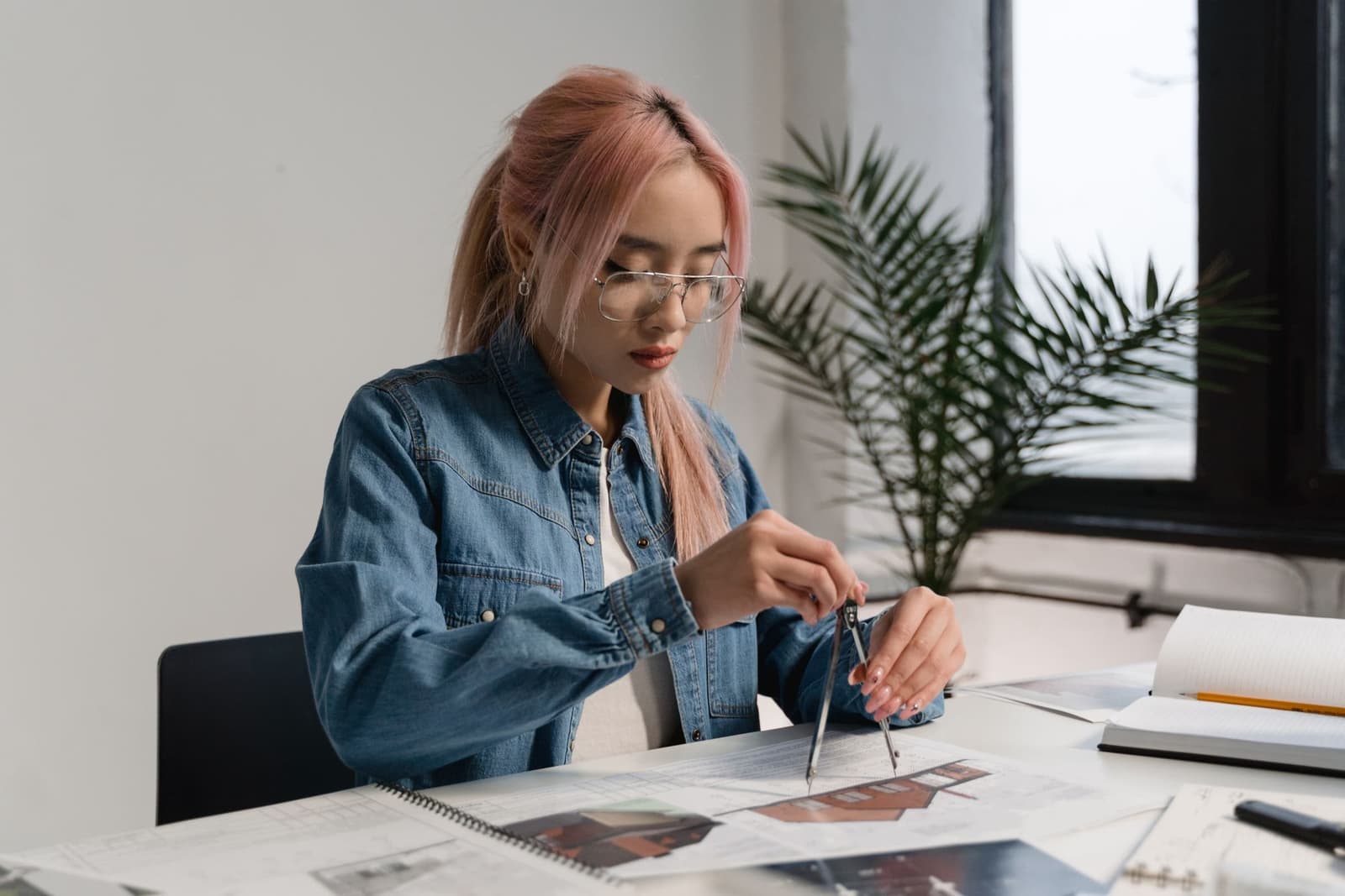 Clara Vale at a desk, working over plans with a compass.