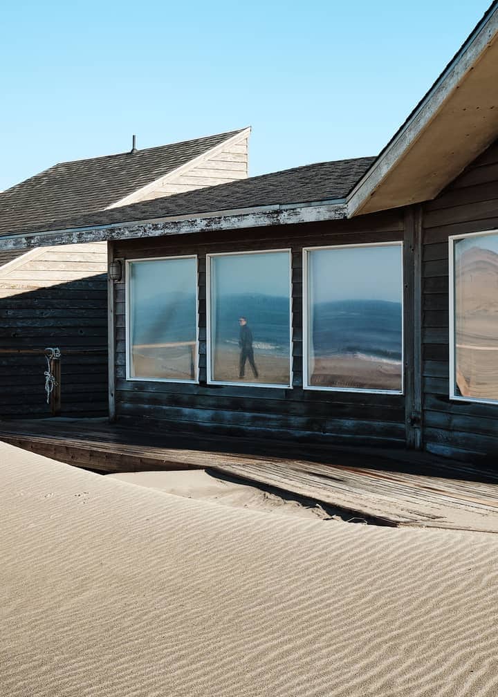 House 2: dark charred-timber walls and a long window reflecting the beach.