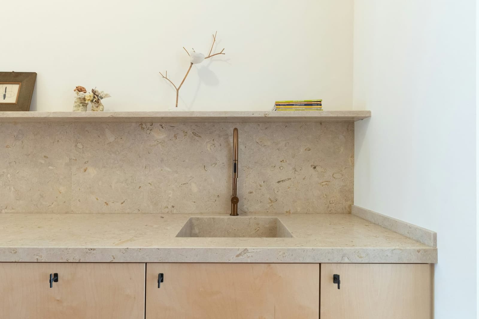 A pale kitchen in honed limestone with a brass tap and open oak shelving.