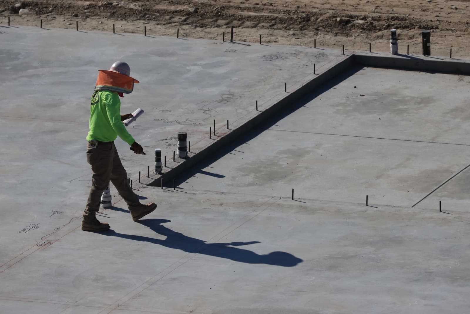 A site worker walking across a fresh concrete slab with the house's set-out lines marked on it.